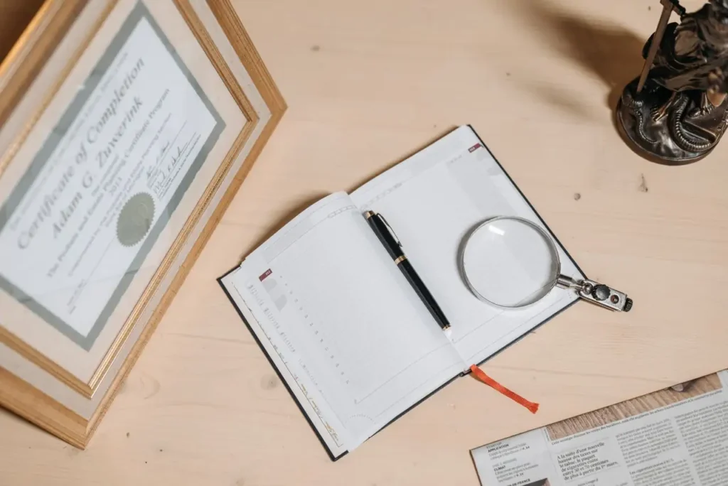 Escritorio con un certificado enmarcado, una libreta y una lupa