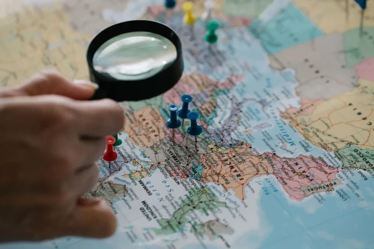 Lupa sobre un mapa del mundo con chinchetas de colores