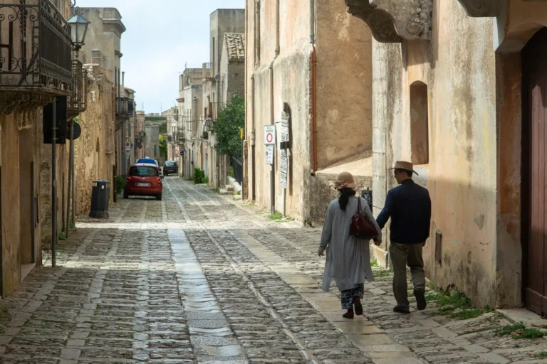 Arraigo social: pareja paseando por una calle empedrada de un pueblo mediterráneo