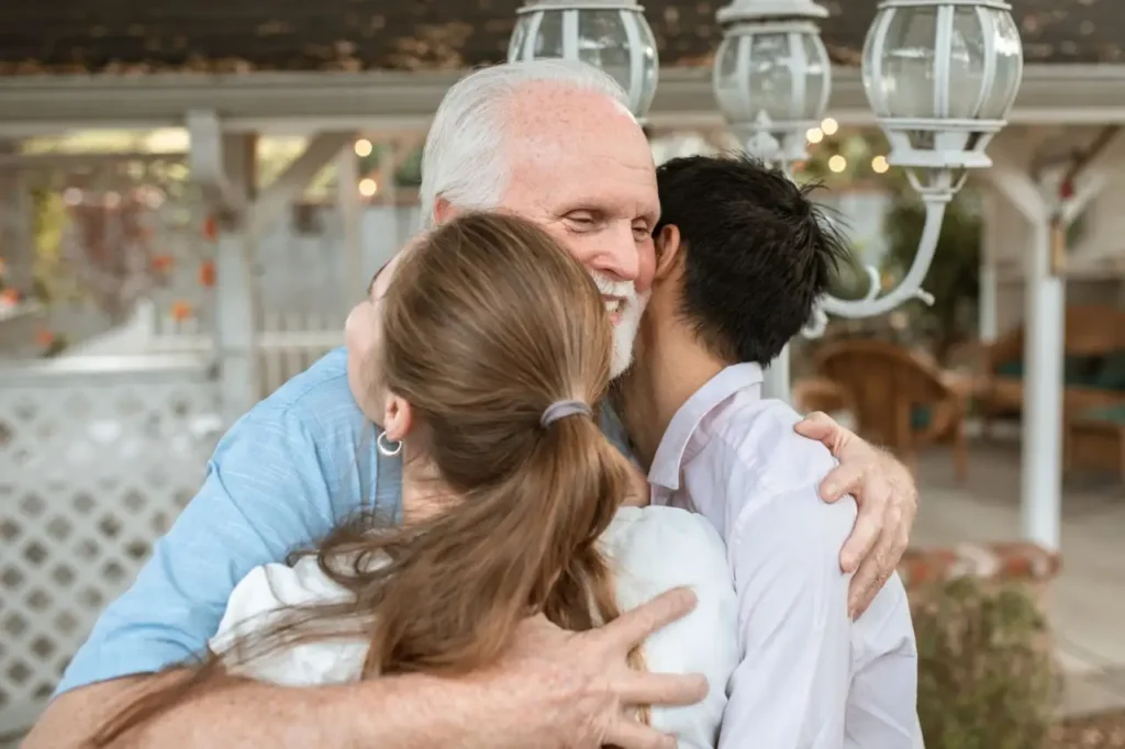 Hombre mayor abrazando a dos jóvenes en un reencuentro familiar